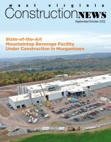 Aerial view of a large beverage facility under construction surrounded by autumn trees, with parked vehicles and construction equipment in Morgantown.