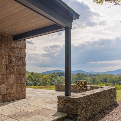 A patio with stone walls overlooks a scenic landscape of rolling hills under a cloudy sky, creating a serene outdoor setting.