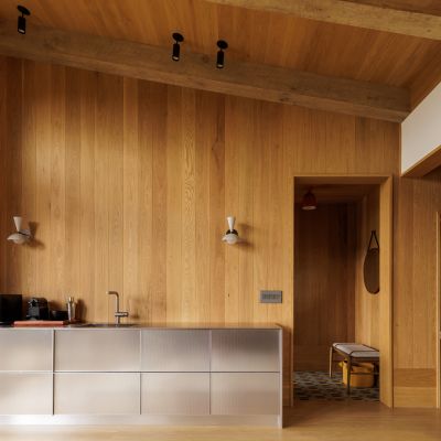 Modern kitchen with wood paneling, stainless steel cabinets, and minimal decor. Includes a microwave, small sink, and a landscape painting on the wall.