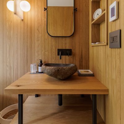 Wood-paneled bathroom with modern fixtures, stone basin, wall mirror, and subtle lighting. Open shelving and basket add natural, minimalist charm.