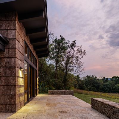 Modern house exterior with wooden siding at sunset, overlooking a scenic landscape with trees and open sky. Calm and serene ambiance.