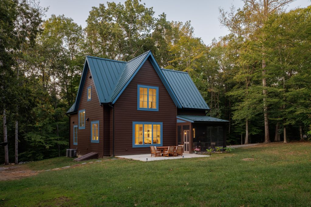 The house glows quietly in the forest as the daylight fades into dusk.