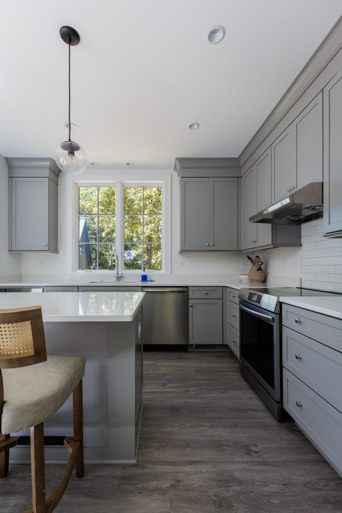 Interior of the kitchen with neutral gray tones, sunlight, and views of the trees outside the window.