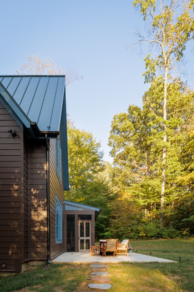 Side view of the home with patio furniture and trees beyond.